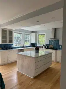 A custom kitchen redesign with white cabinets, granite countertops, and blue textured tile backsplash. L-shaped design.